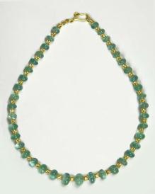 Ligh colored emeralds and gold bead necklace laid flat on white surface