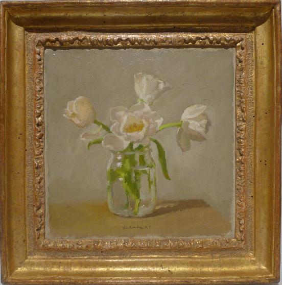 White flowers on glass jar on table in front of grey wall in ornate gold frarme