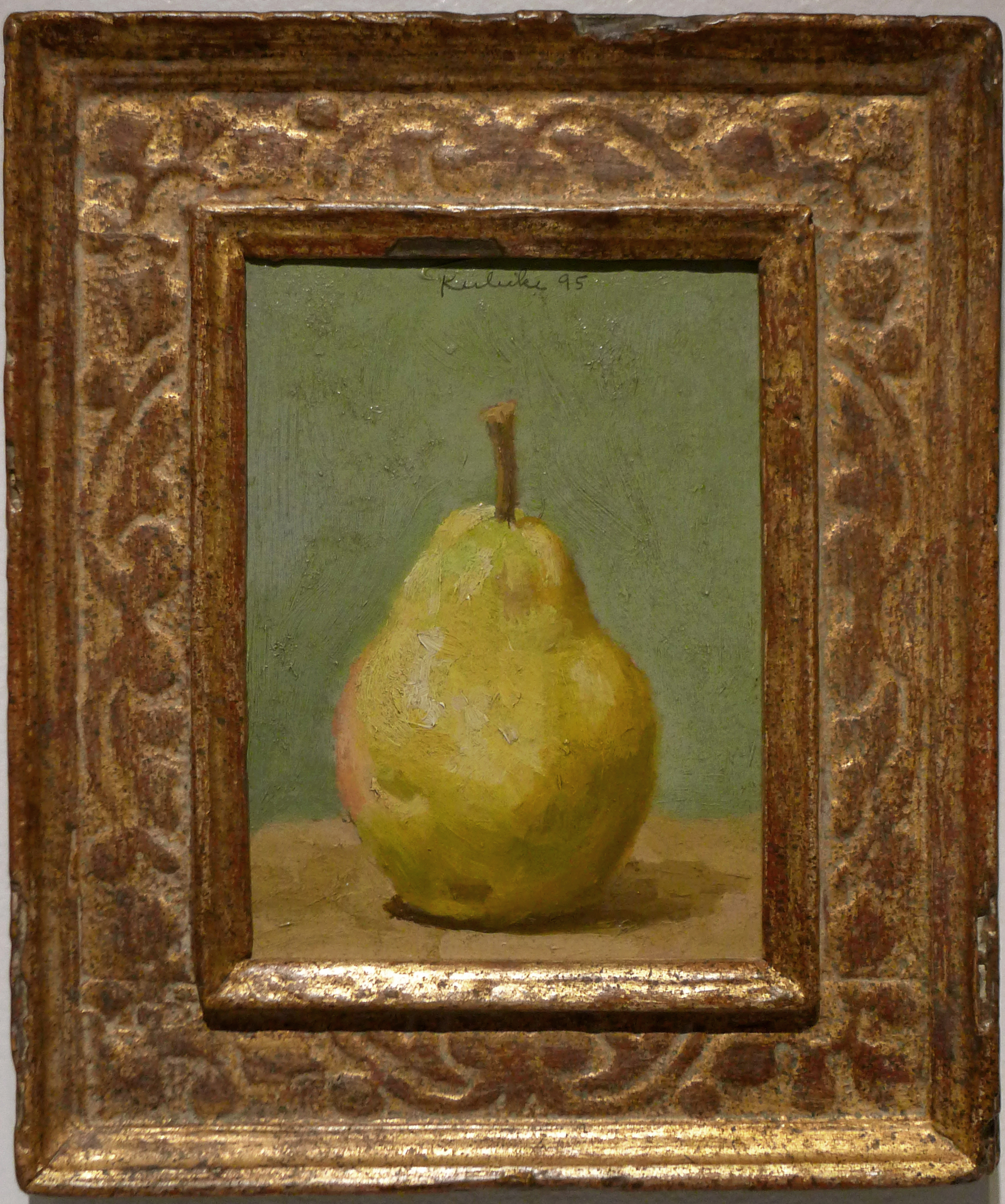 Green pear on table in frront of grreen wall in ornate gold farme