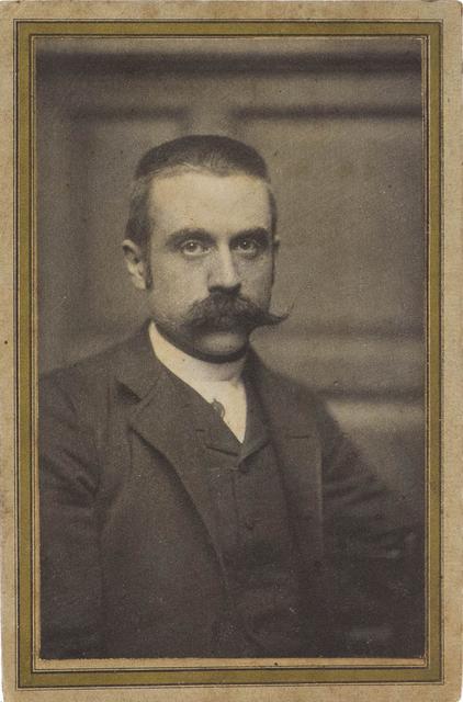 Man with large mustache seated in front of doorway