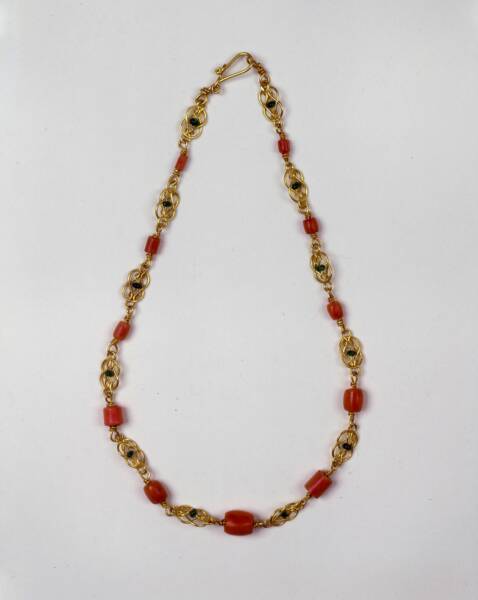 Coral and gold beads with emeralds in a necklace, clasped, laid flat on white background