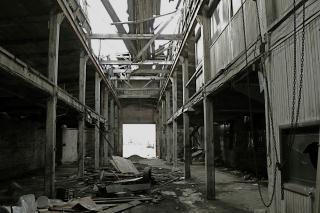 Decaying factory building with rubble at center and grey beams and walls with open roof