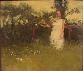 Woman in white dress standing in grassy filed in front of red wooden structure with hand touching branch