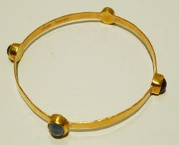 Gold bracelet with four blue stones laying flat on white ground