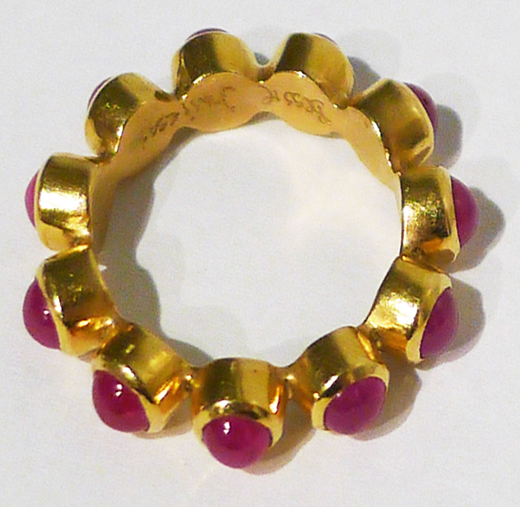 Ring of gold segments with magenta stones laid flat on white ground