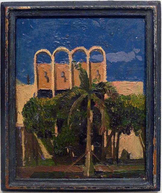 Tan building with palm tree in front with other trees behind and blue sky in black frame