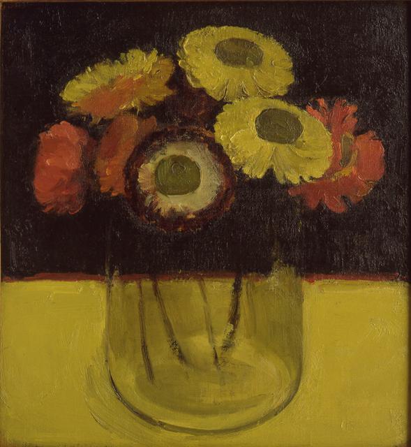 Yellow, red, and burgundy flowers in glass vase on yellow table in front of black wall