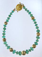 Emerald beads with gold bead necklace, clasped and laid flat on white ground