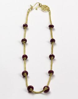 Gold necklace with magenta ruby beads laid flat in a long oval shape on white background