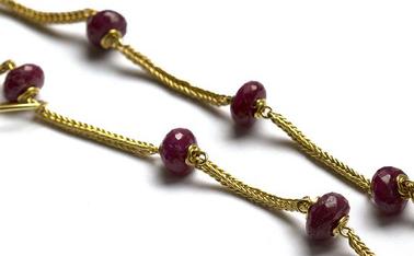 Close up shot of gold necklace with magenta sapphire beads on white background