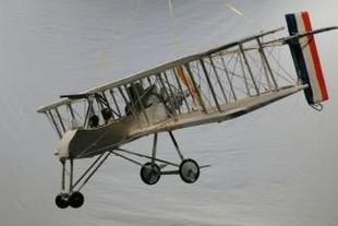 Grey airplane with four wheels and red white and blue stripes on right suspended from strings and pointing left and down