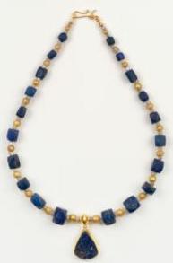 Blue and gold beads with blue stone pendant at bottom center, laid flat on white background