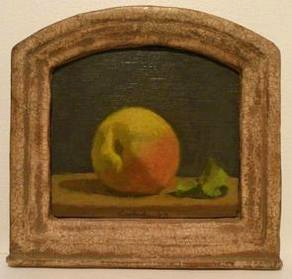 Yellow and orange peach at center with single green leaf at right on brown table in front of black wall in ornate frame