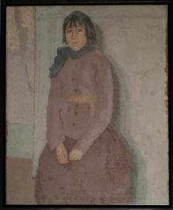 Woman with short hair and bangs wearing blue scarf and mauve dress in front of grey wall