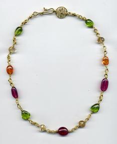 Gold necklace with green, yellow, orange, and purple beads laid flat on white ground