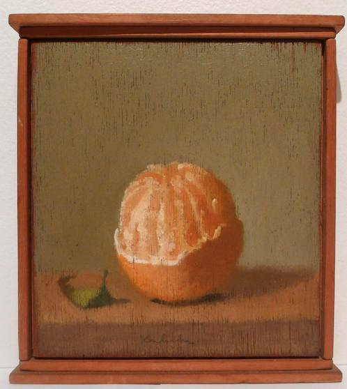 Half peeled orange with peel at bottom and green leaf at lower left on table in wood frame