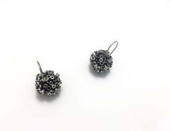 Twin mettallc balls made of small metal pieces and earring back loops laid flat off center on white ground