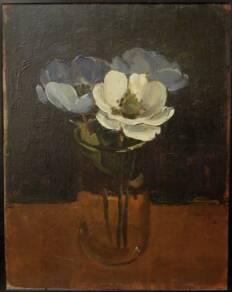 Two blue and one white flower in class jar on brown table in gront of black wall